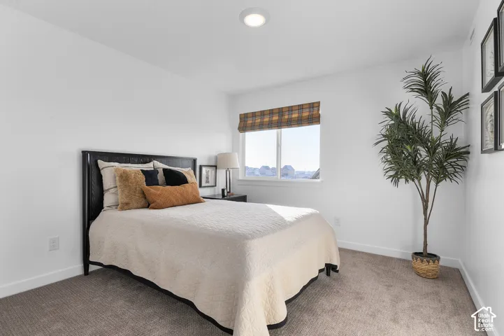 Recessed ceiling lighting, window with plaid roller shade, dark wood headboard, dark wood nightstand, and neutral carpet flooring