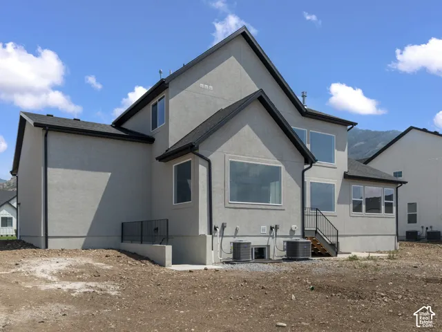 Stucco exterior featuring multiple windows, dark roof, black gutters, and exterior staircase