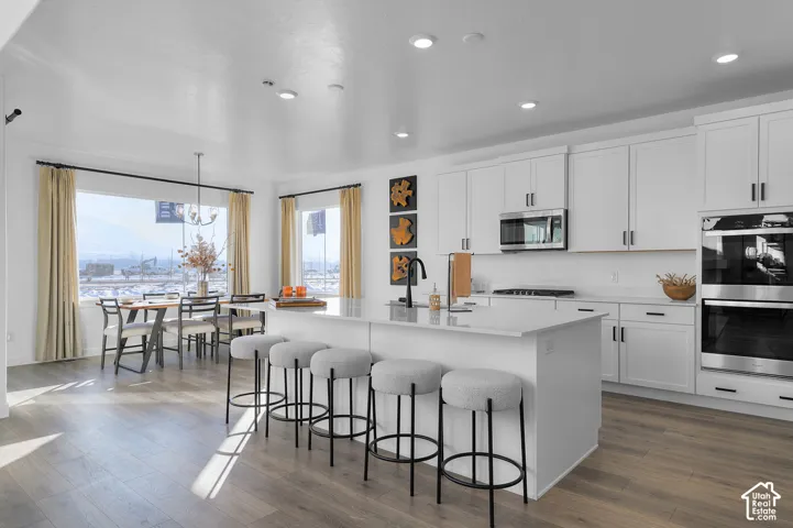Spacious open-concept kitchen featuring a large island with seating, white shaker cabinetry, stainless steel appliances, and wood-finish flooring