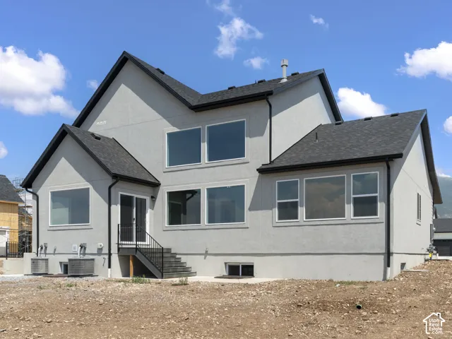 Stucco exterior with multiple large windows, dark shingle roof, black gutters, and a rear entrance with black metal railing