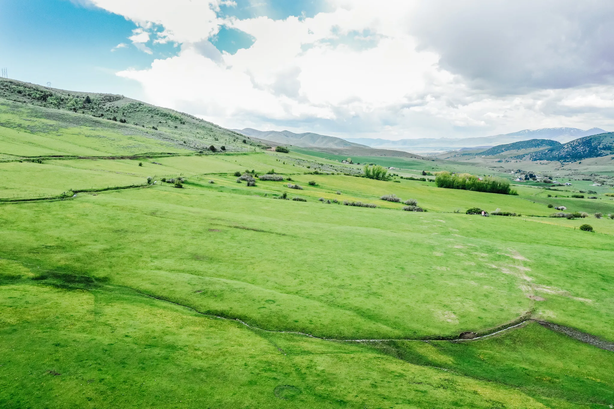 Expansive green hills with natural terrain, distant mountains, and scattered trees
