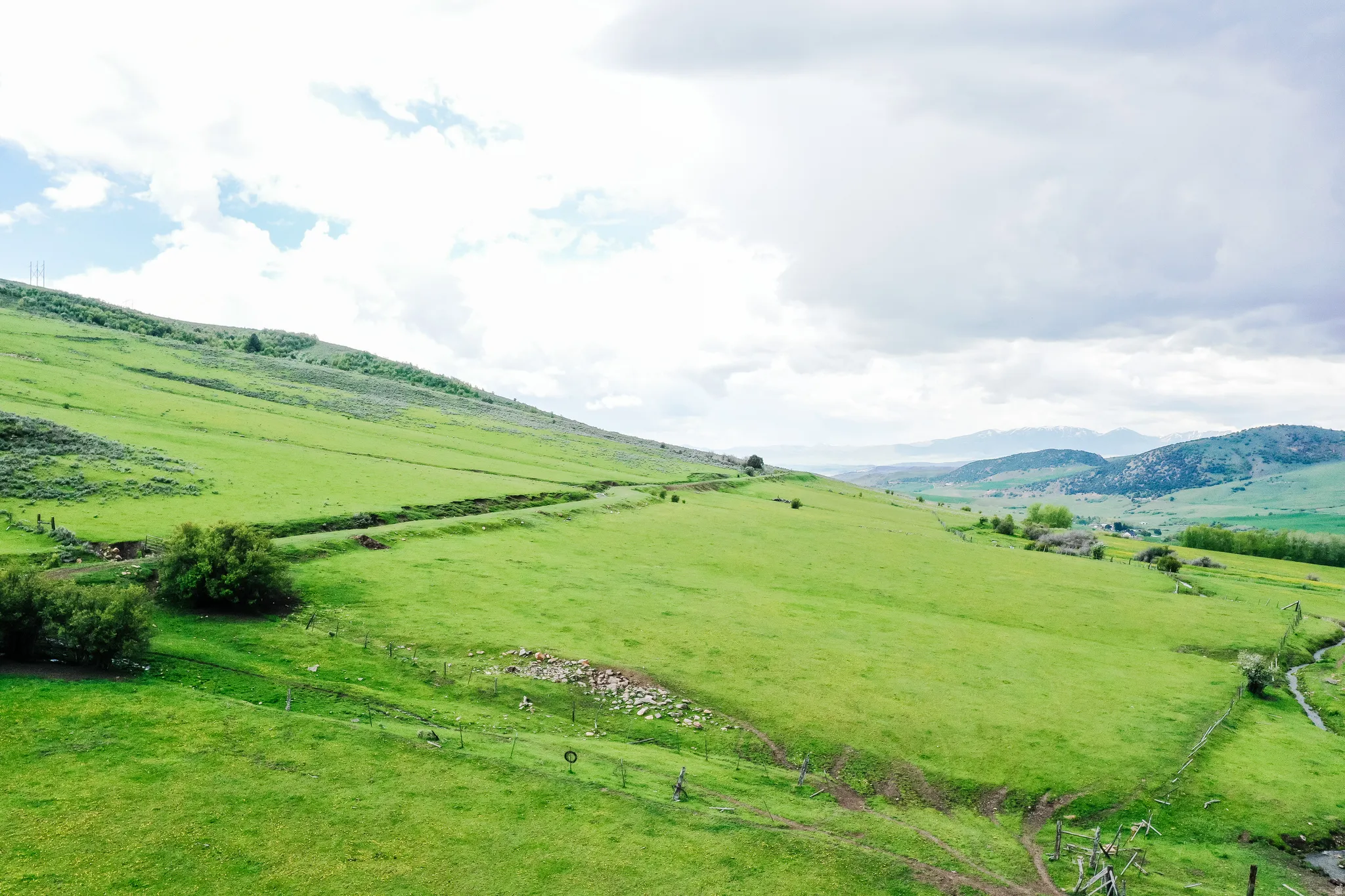 Expansive green landscape with rolling hills, a distant mountainous backdrop, and mature trees