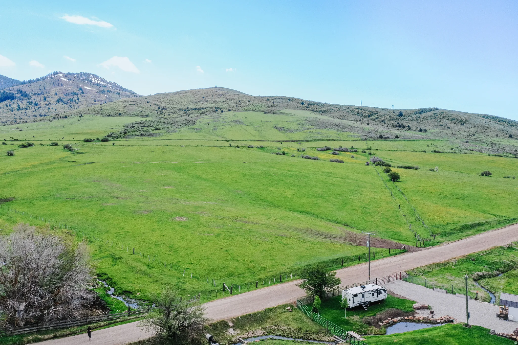 Expansive green acreage with distant mountains, a gravel road, and a paved driveway