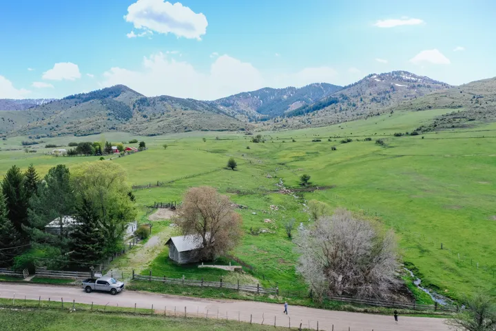 Expansive green landscape with distant mountains, featuring a dirt road, wood fence, and mature trees
