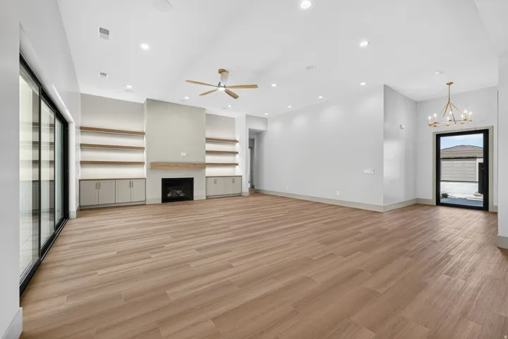 Expansive living space featuring wood-finish flooring, a contemporary fireplace with a wood mantle, built-in cabinetry, and open shelving