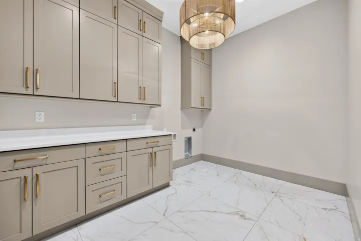 Extensive cabinetry with gold-finish hardware, white countertop, white marble-look tile flooring, and a decorative ceiling light fixture