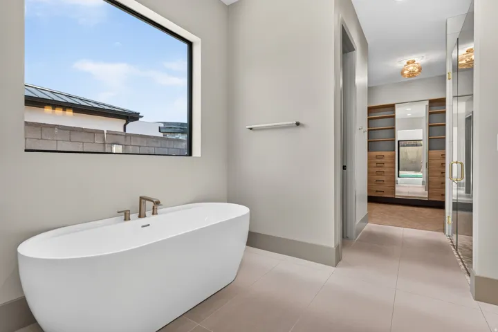 Freestanding soaking tub with brushed nickel fixtures, large picture window, and neutral tone tile flooring
