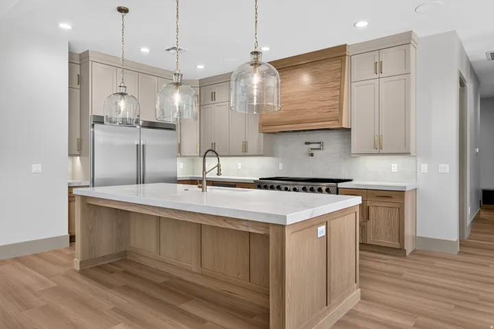 Kitchen featuring an expansive island with a light-toned countertop, wood-finish flooring, stainless steel appliances, and ceiling-mounted pendant lighting