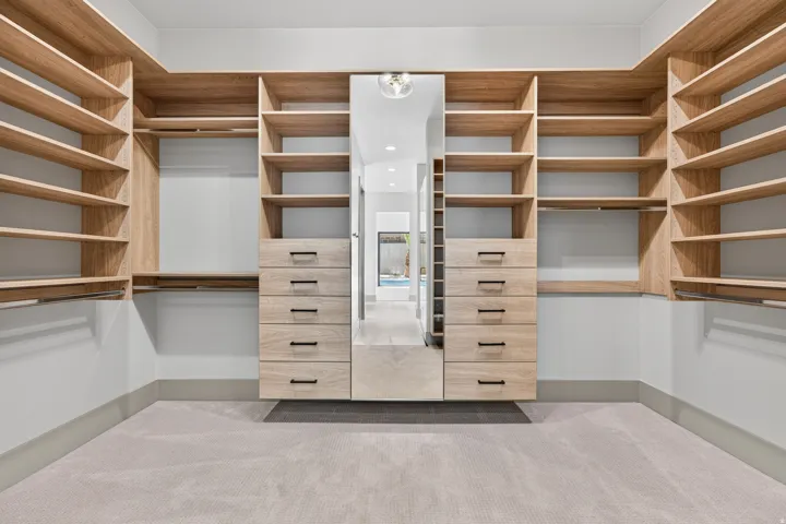 Custom closet system featuring extensive wood-finish shelving, multiple hanging rods, and integrated drawer units with matte black hardware
