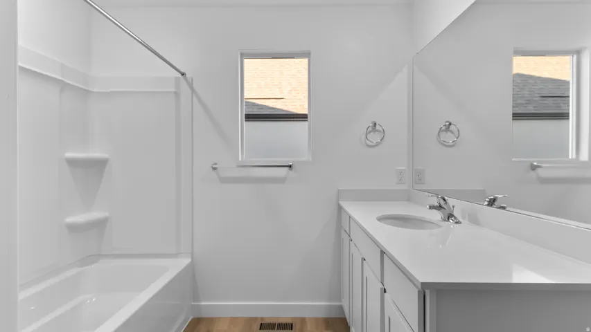 Bathroom with wood-finish flooring, a white vanity, a single undermount sink, and a white bathtub with a built-in shower surround