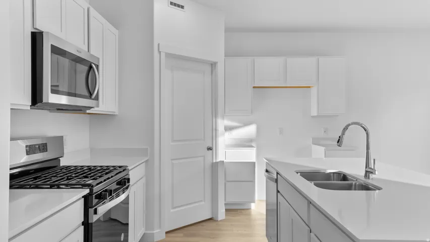 Kitchen featuring a stainless steel microwave, gas range, dual basin sink with a high-arch faucet, white shaker cabinetry, and light-toned flooring