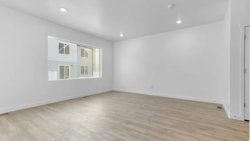 Recessed lighting, light wood-finish flooring, white walls, and a large window