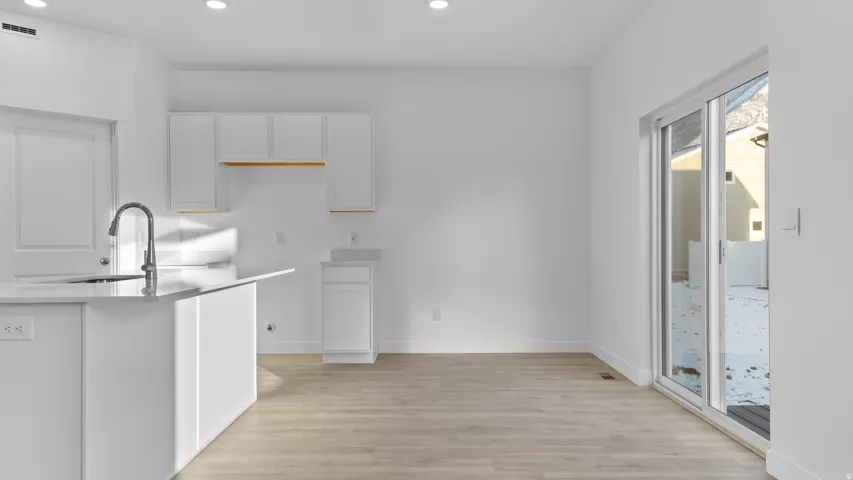 Kitchen featuring white cabinetry, a kitchen island with an integrated sink and gooseneck faucet, light wood-finish flooring, and recessed lighting