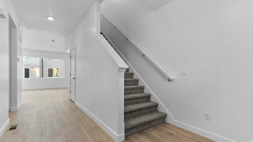 Neutral white wall finishes, wood-finish flooring, carpeted stairs, recessed ceiling lighting, and a prominent window feature