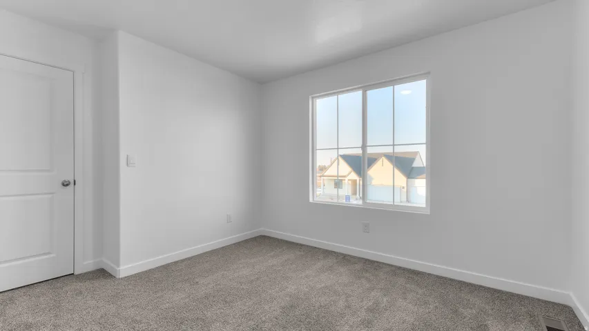 Bright room with a large window, gray carpeting, a white two-panel door, and white trim