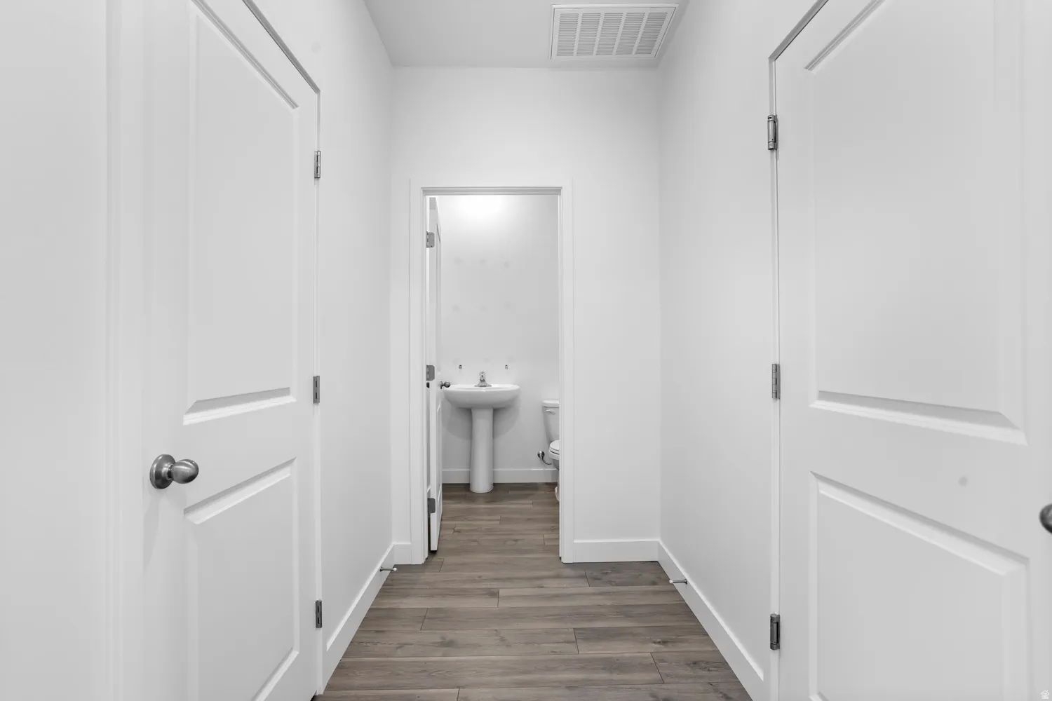 White interior doors, wood-finish flooring, and a pedestal sink with a white toilet