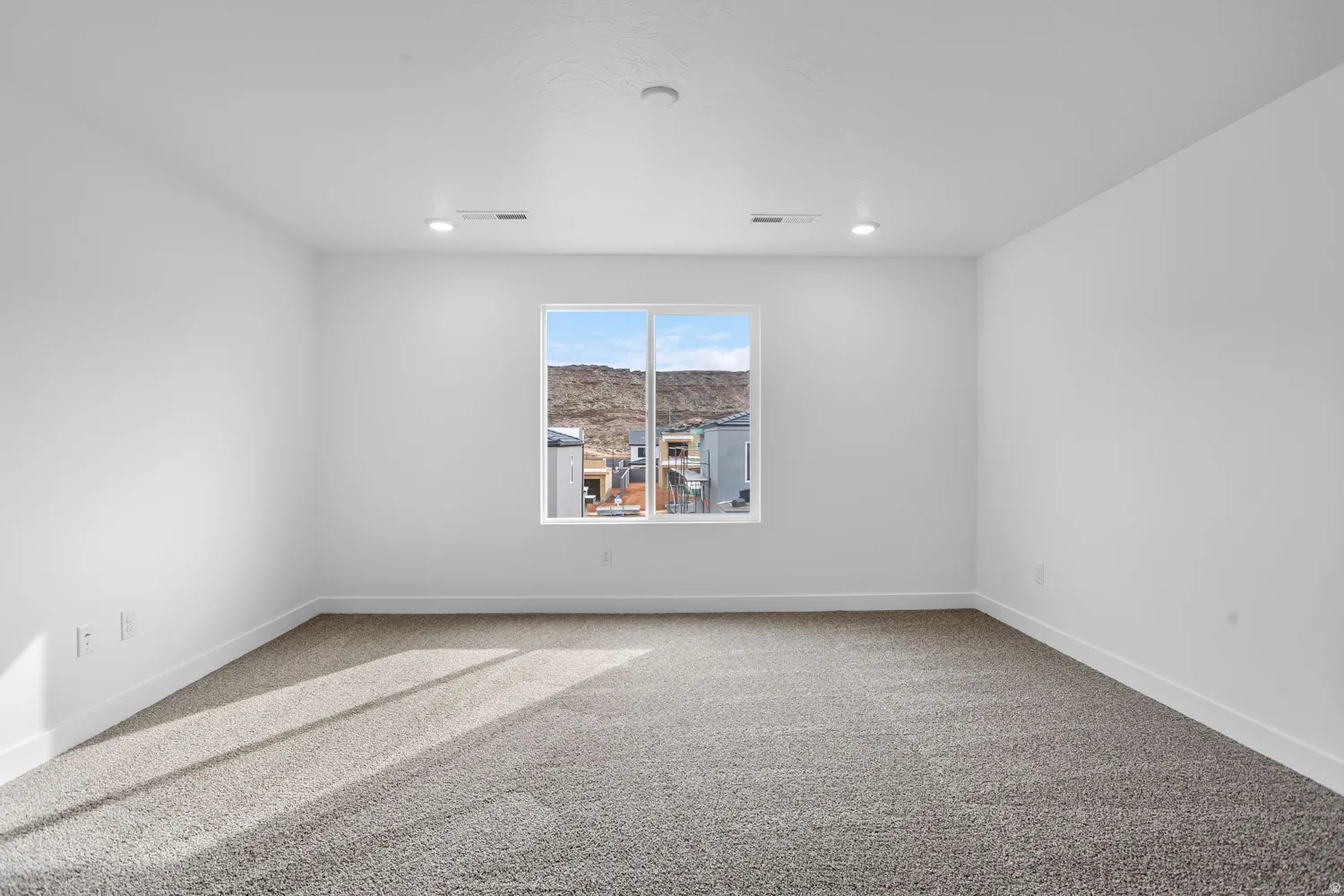 Recessed lighting, large window, neutral carpet, white walls, and mountain scenery