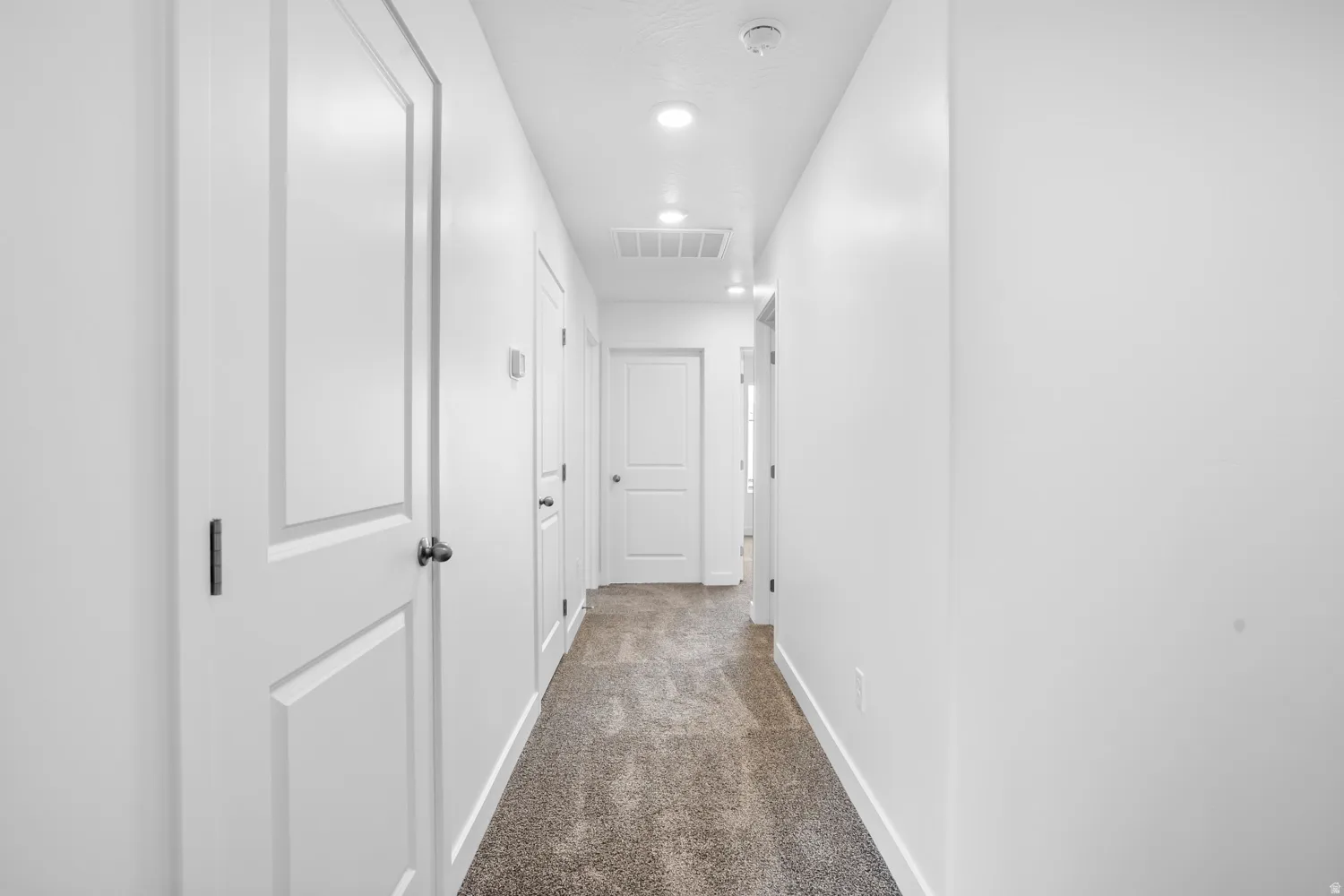 Recessed lighting illuminates a neutral color palette with white walls and soft gray carpeting