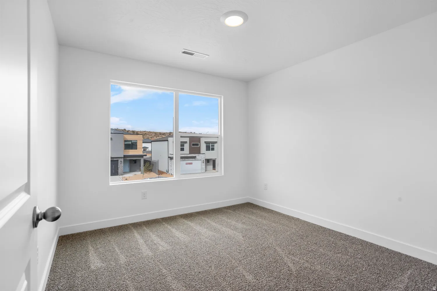 Recessed lighting, large window with white trim, gray patterned carpet, white walls, and white trim