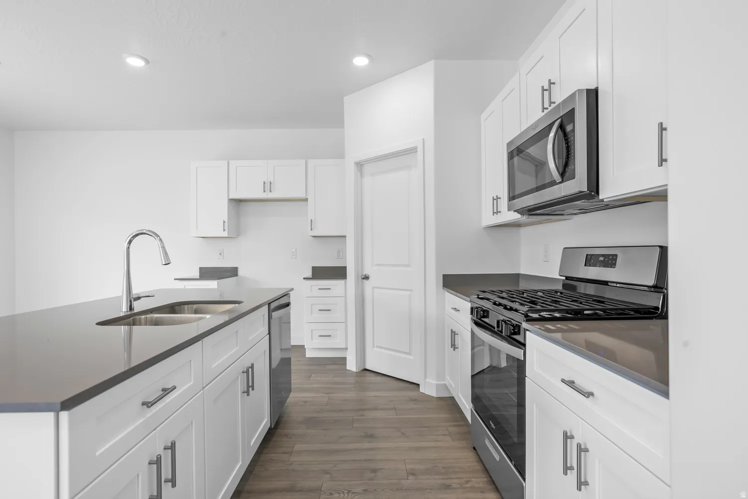 Kitchen featuring an island with double sink, stainless steel appliances, white cabinetry, and wood-finish flooring