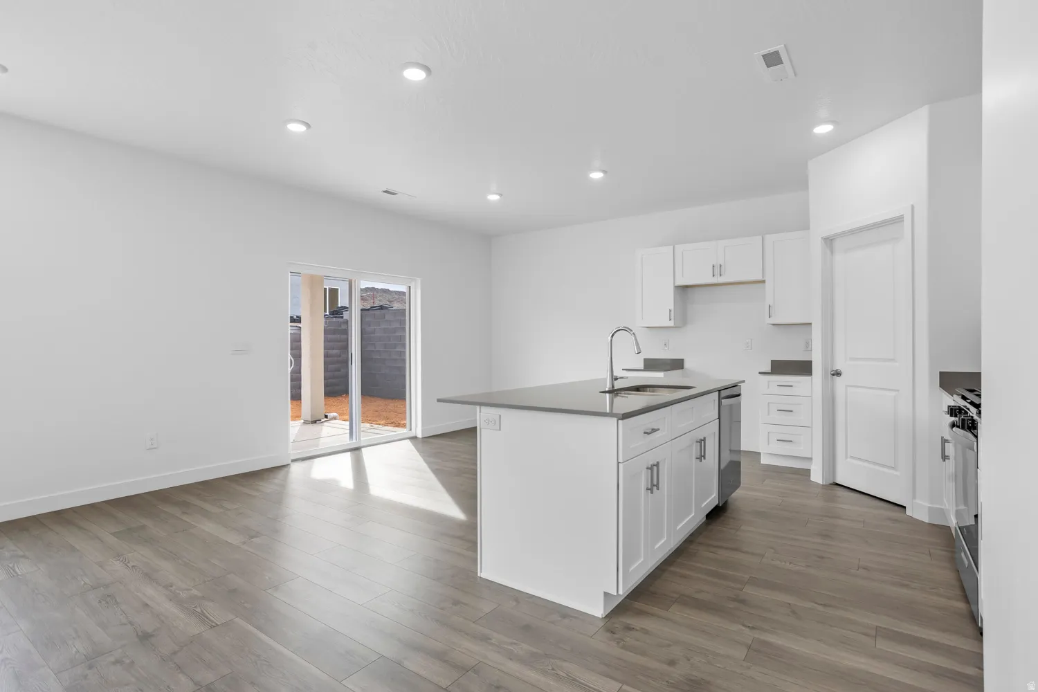 Open-concept living space featuring wood-finish flooring, recessed lighting, and a kitchen island with a stainless steel sink