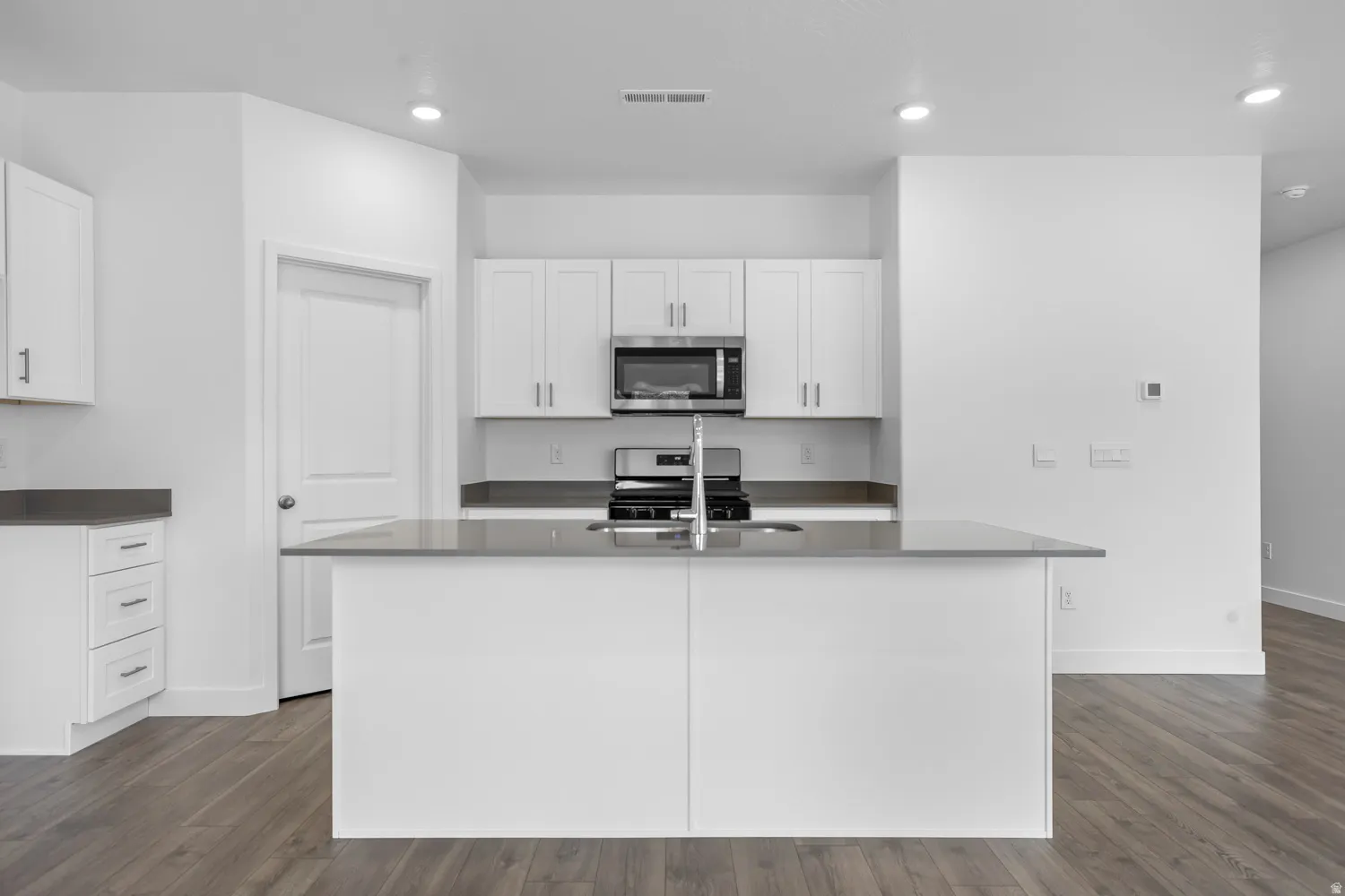Kitchen featuring white cabinetry, gray countertops, stainless steel appliances, and a central island with an integrated sink