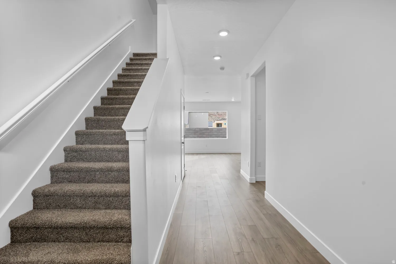 Carpeted staircase with white handrail and newel post, wood-finish flooring, recessed lighting, and white walls throughout