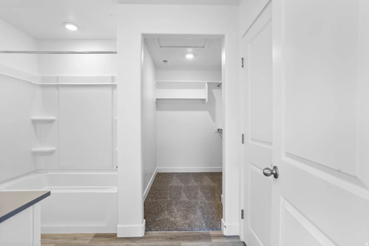 White paneled doors with brushed nickel hardware, white tub/shower combination with built-in shelving, wood-finish flooring, recessed lighting, and carpeted closet with built-in shelving