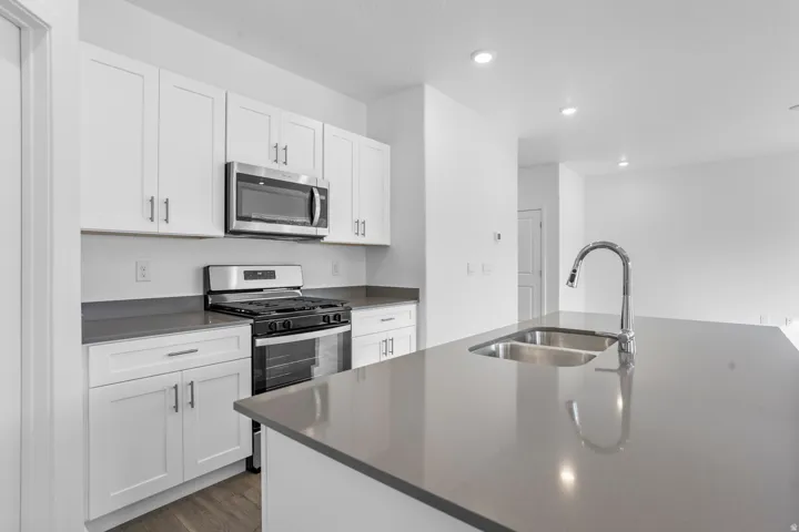 Kitchen featuring an island with a dual basin sink and gooseneck faucet, white shaker cabinetry, stainless steel appliances, and recessed lighting