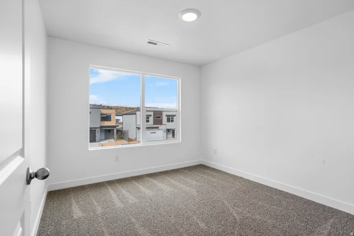 Recessed lighting, large window with white trim, gray patterned carpet, white walls, and white trim
