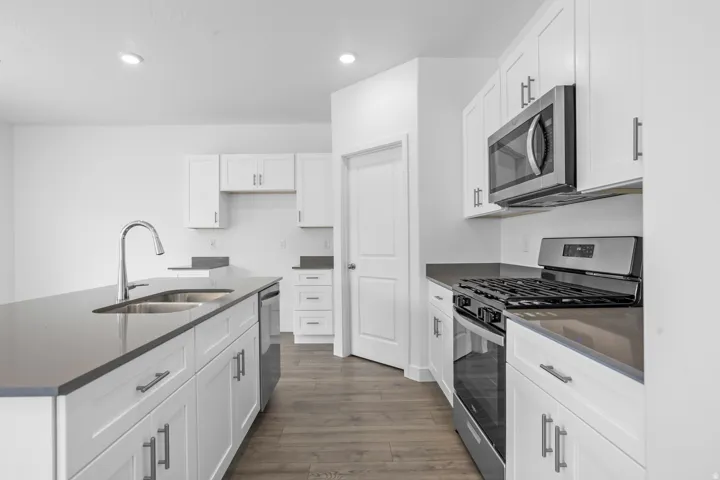 Kitchen featuring an island with double sink, stainless steel appliances, white cabinetry, and wood-finish flooring