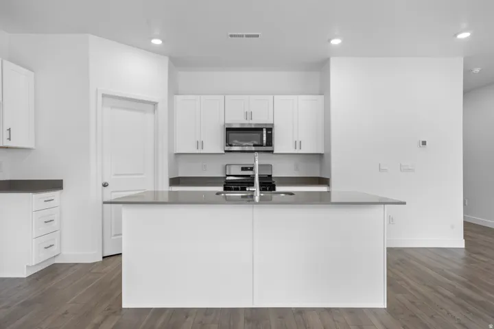 Kitchen featuring white cabinetry, gray countertops, stainless steel appliances, and a central island with an integrated sink