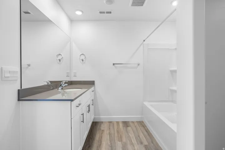 Modern bathroom featuring a single vanity with a solid surface countertop, integrated sink, large wall-mounted mirror, and a full-size bathtub with a shower surround