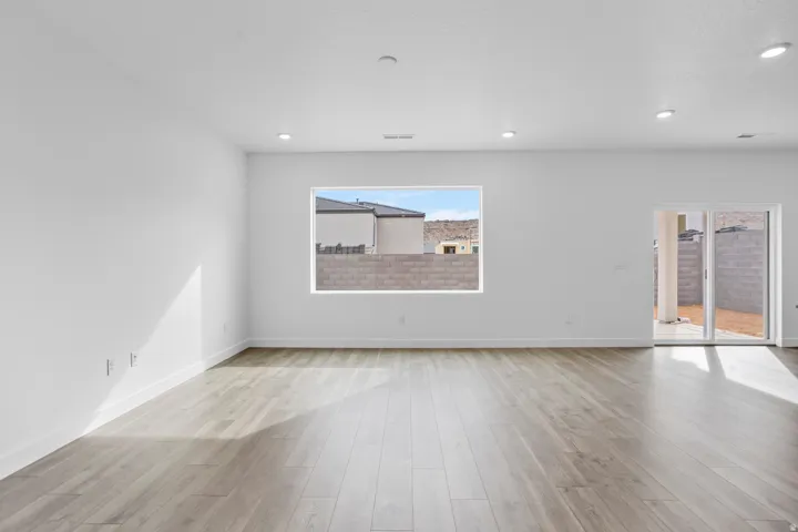 Spacious room featuring wood-finish flooring, recessed lighting, a large window, and a sliding glass door
