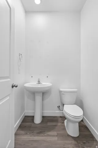White pedestal sink with chrome faucet, a white toilet, and wood-finish flooring