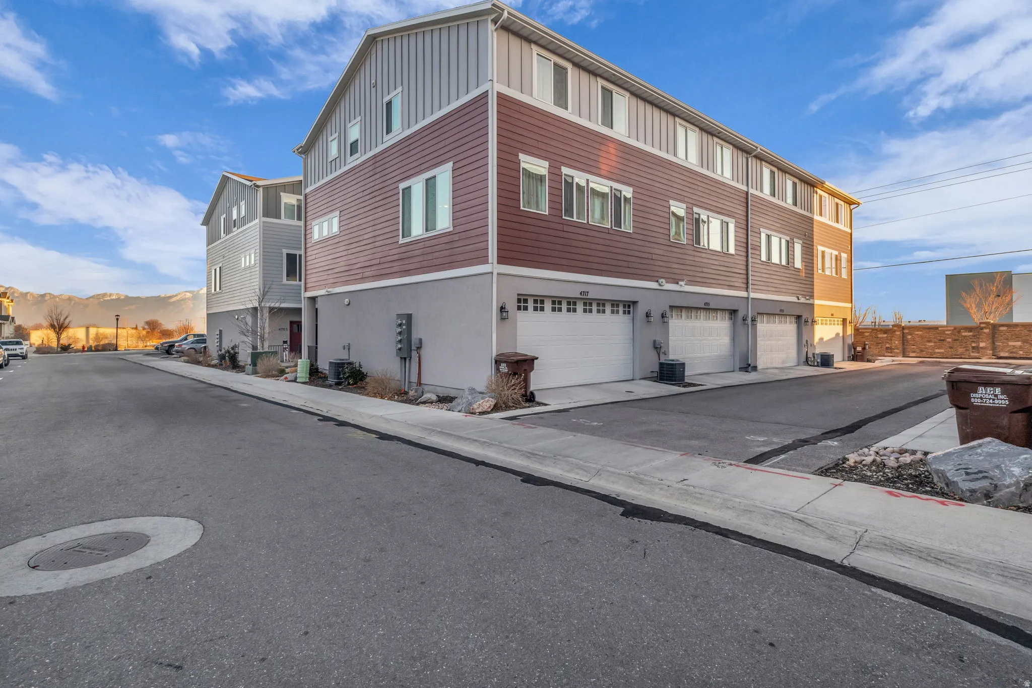 Three-story exterior with horizontal siding, multiple windows, and individual garage doors