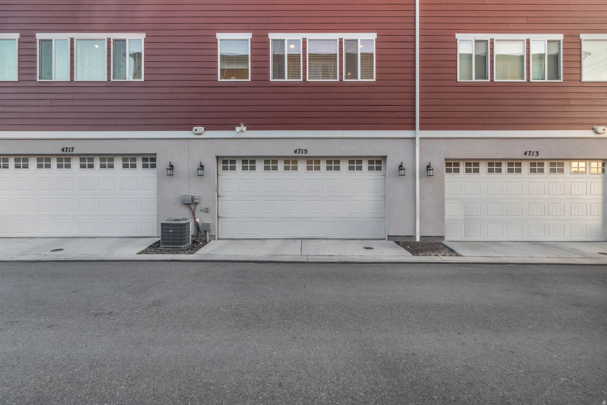 Red horizontal siding, white panel garage doors, concrete driveways, and exterior wall lanterns