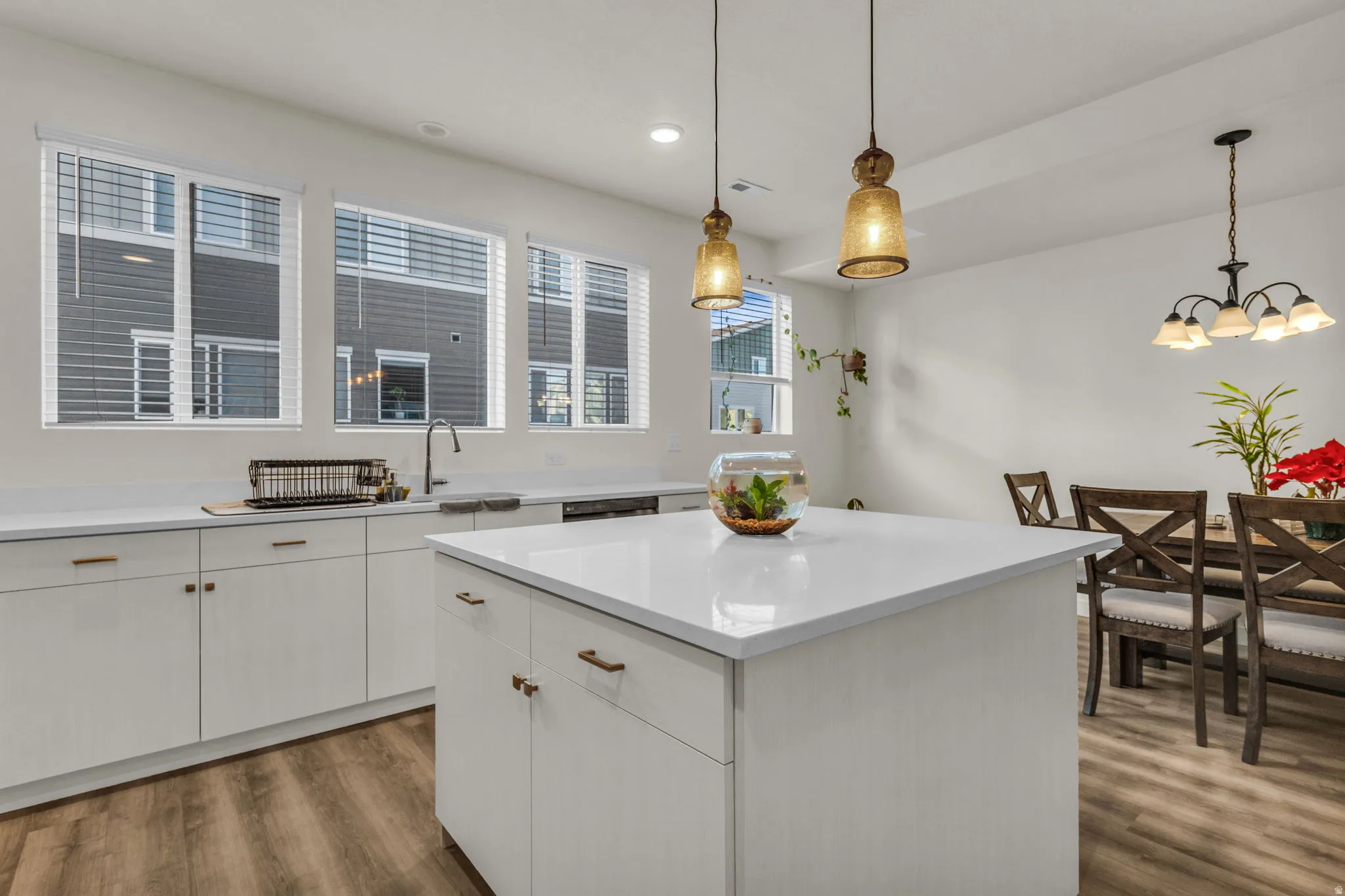 Kitchen with a central island, wood-finish flooring, white cabinetry, integrated sink, and pendant lighting