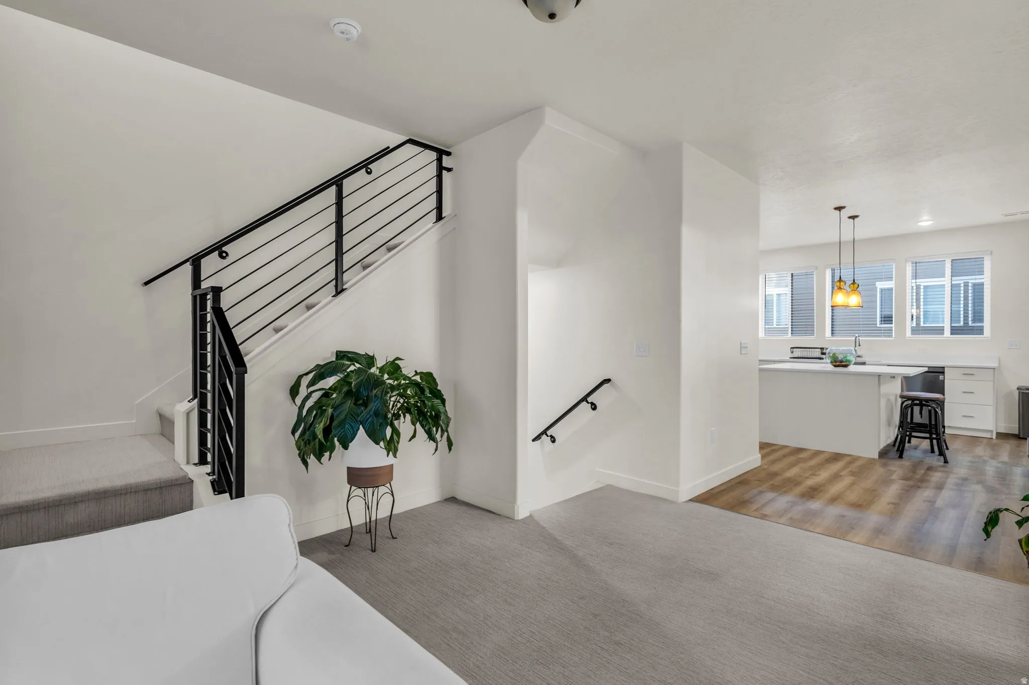 Contemporary black metal stair railing, light-toned carpeted flooring, wood-finish flooring, white cabinetry, and a kitchen island with pendant lighting