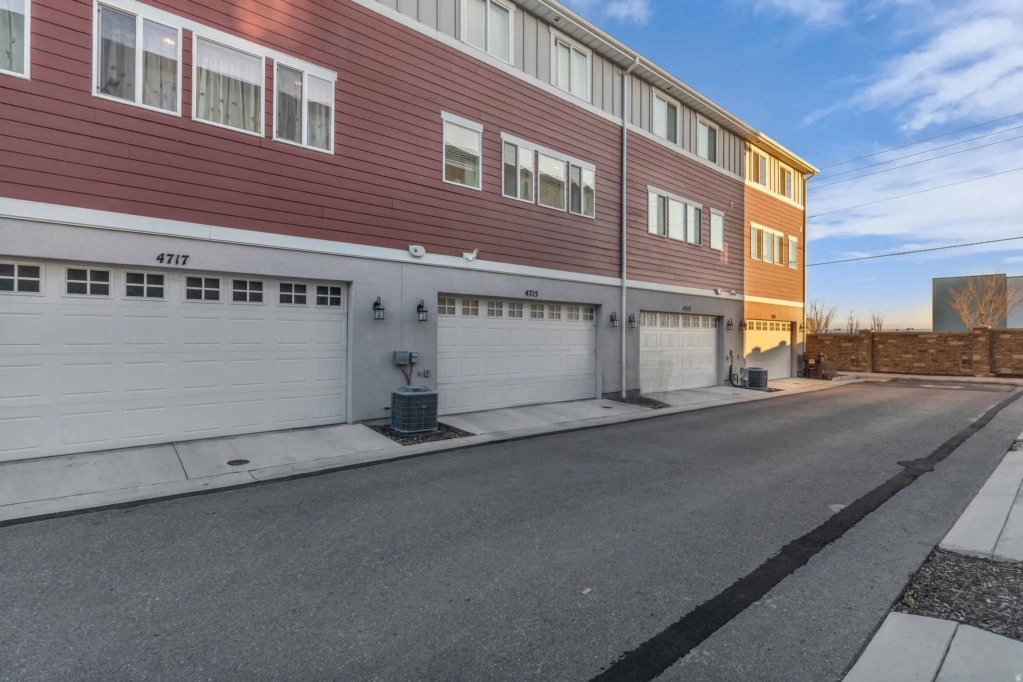Multi-level structure featuring red horizontal siding, multiple white-framed windows, and white garage doors with window inserts