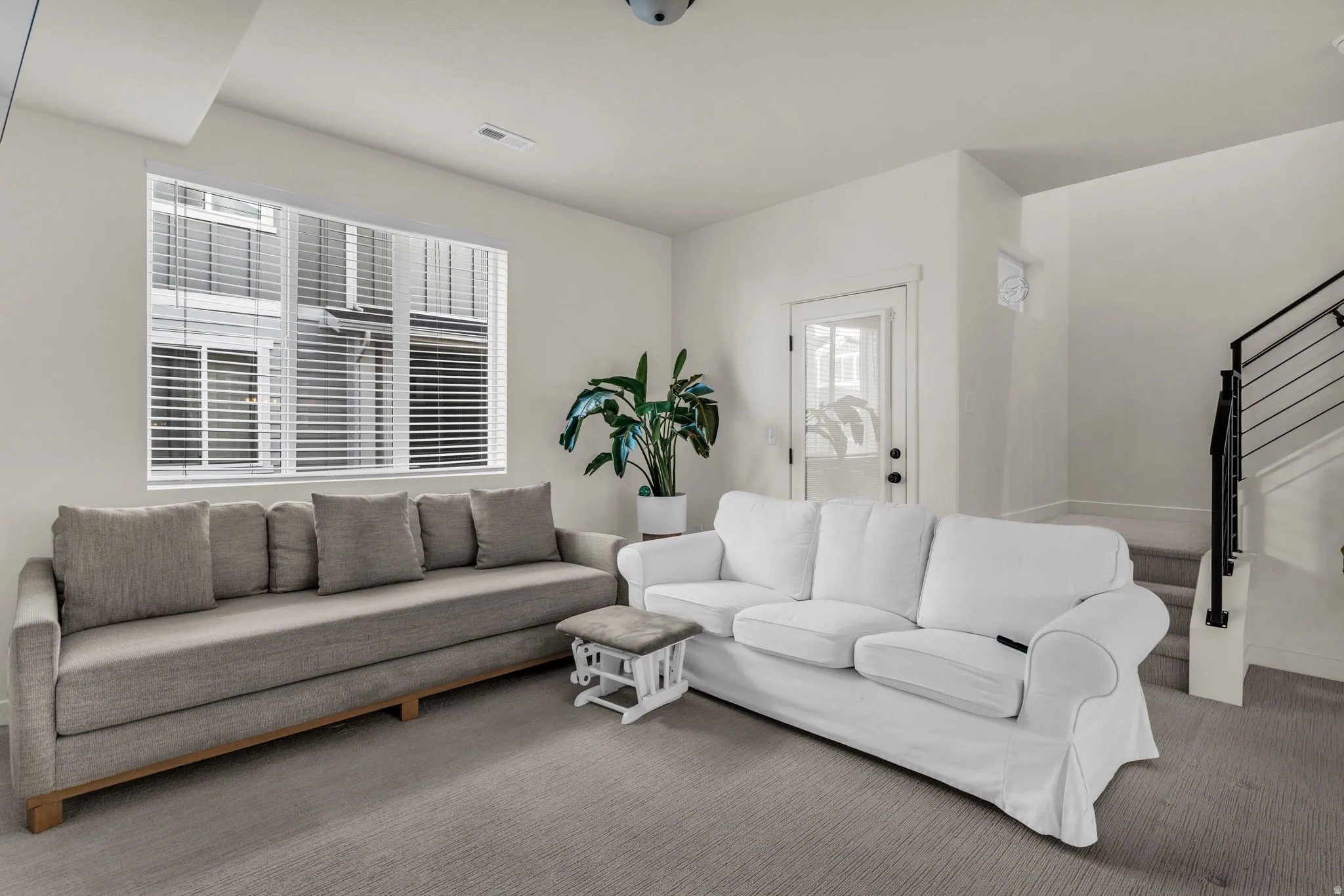 Neutral wall paint, light-toned carpet flooring, multi-pane window with horizontal blinds, interior door with frosted glass, and a staircase with metal railings