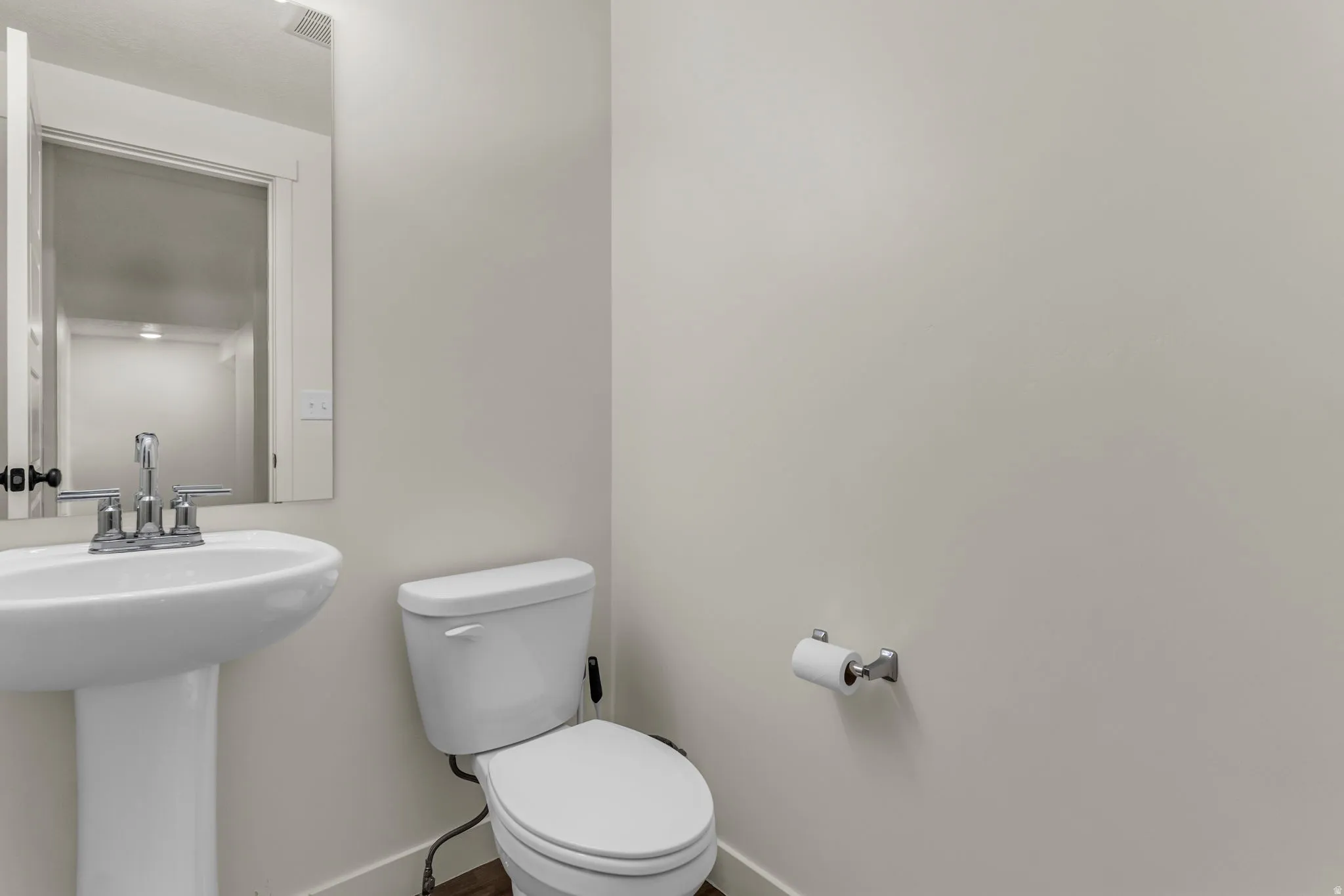 Pedestal sink with chrome faucet, wall-mounted mirror, toilet, and wood-finish flooring