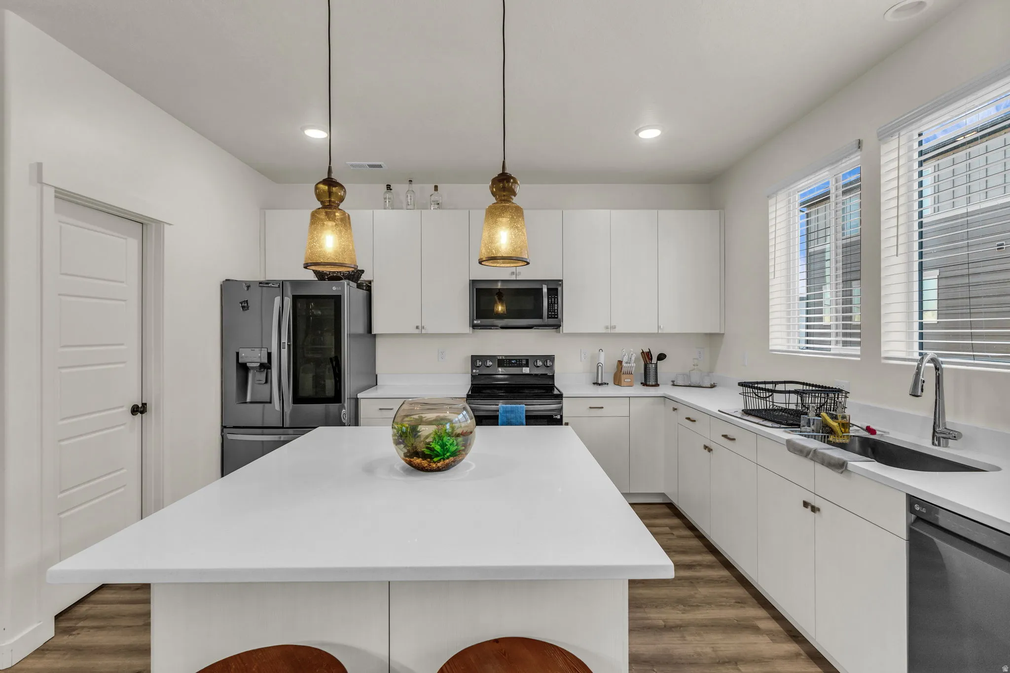 Spacious kitchen featuring a large central island, white cabinetry, integrated stainless steel appliances, and wood-finish flooring