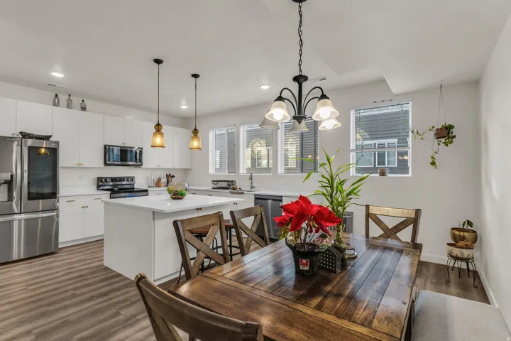 Open-concept kitchen and dining area featuring white cabinetry, stainless steel appliances, a center island, and wood-finish flooring