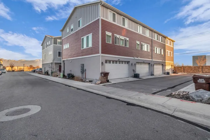 Three-story exterior with horizontal siding, multiple windows, and individual garage doors