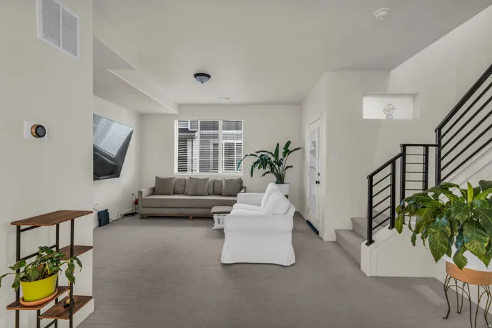 Carpeted living area featuring multiple windows, a modern thermostat, and a staircase with a black metal railing