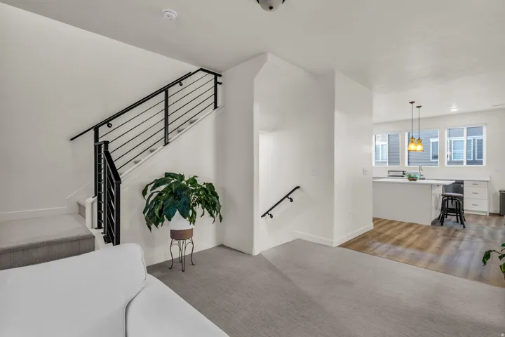Contemporary black metal stair railing, light-toned carpeted flooring, wood-finish flooring, white cabinetry, and a kitchen island with pendant lighting