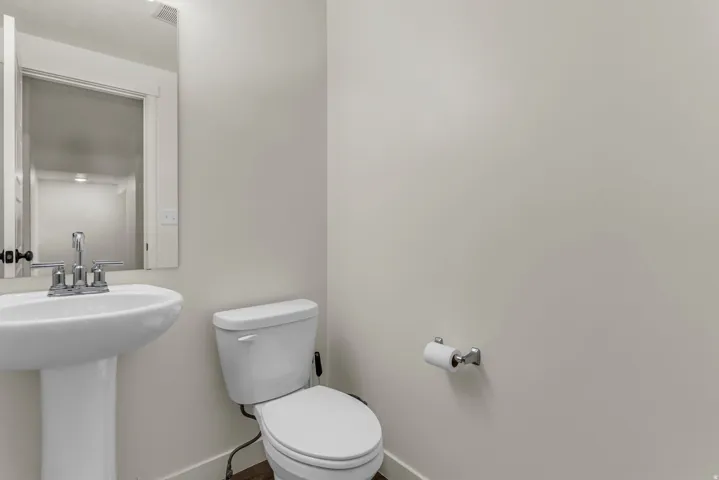 Pedestal sink with chrome faucet, wall-mounted mirror, toilet, and wood-finish flooring