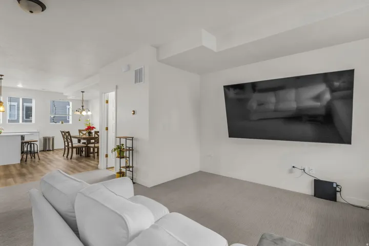 Open-concept living area featuring light-toned carpeting, white walls, and a dedicated dining space with wood-finish flooring