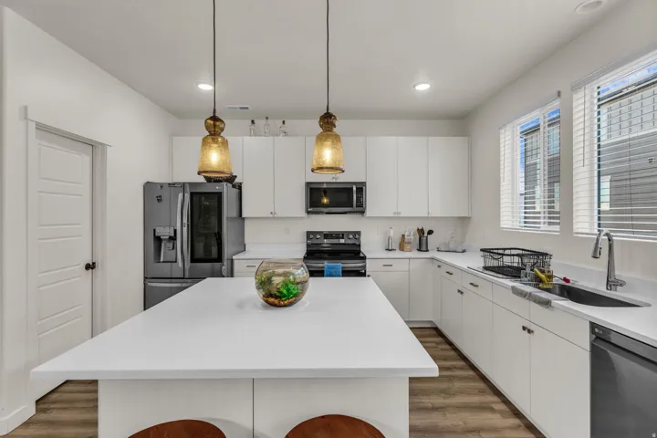 Spacious kitchen featuring a large central island, white cabinetry, integrated stainless steel appliances, and wood-finish flooring